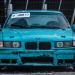 Close-up of a teal BMW drift car on a snow-covered track, emphasizing its rugged, sporty appeal.